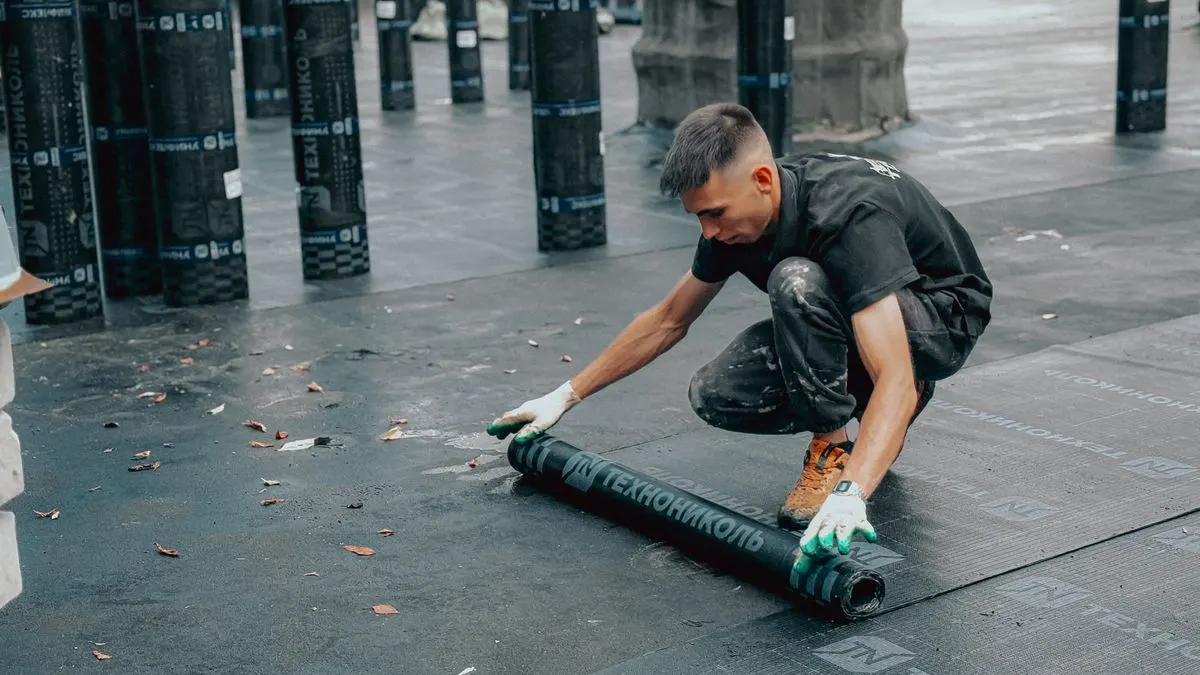 A roofer rolling out a waterproofing membrane