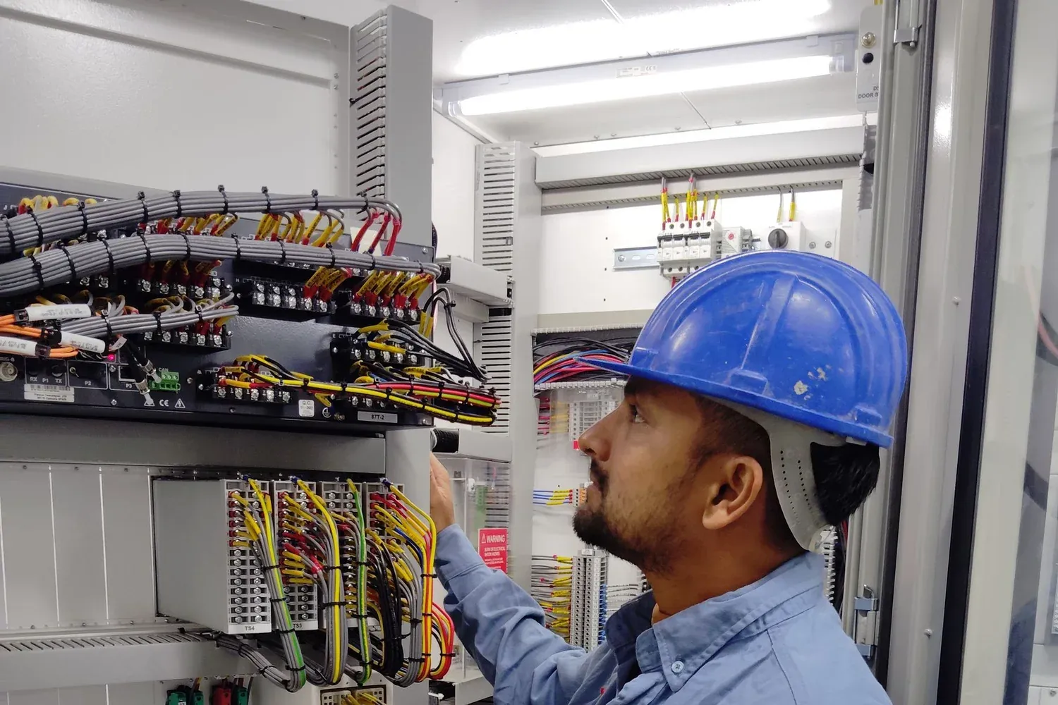 An electrician inspecting wiring inside an electrical control panel