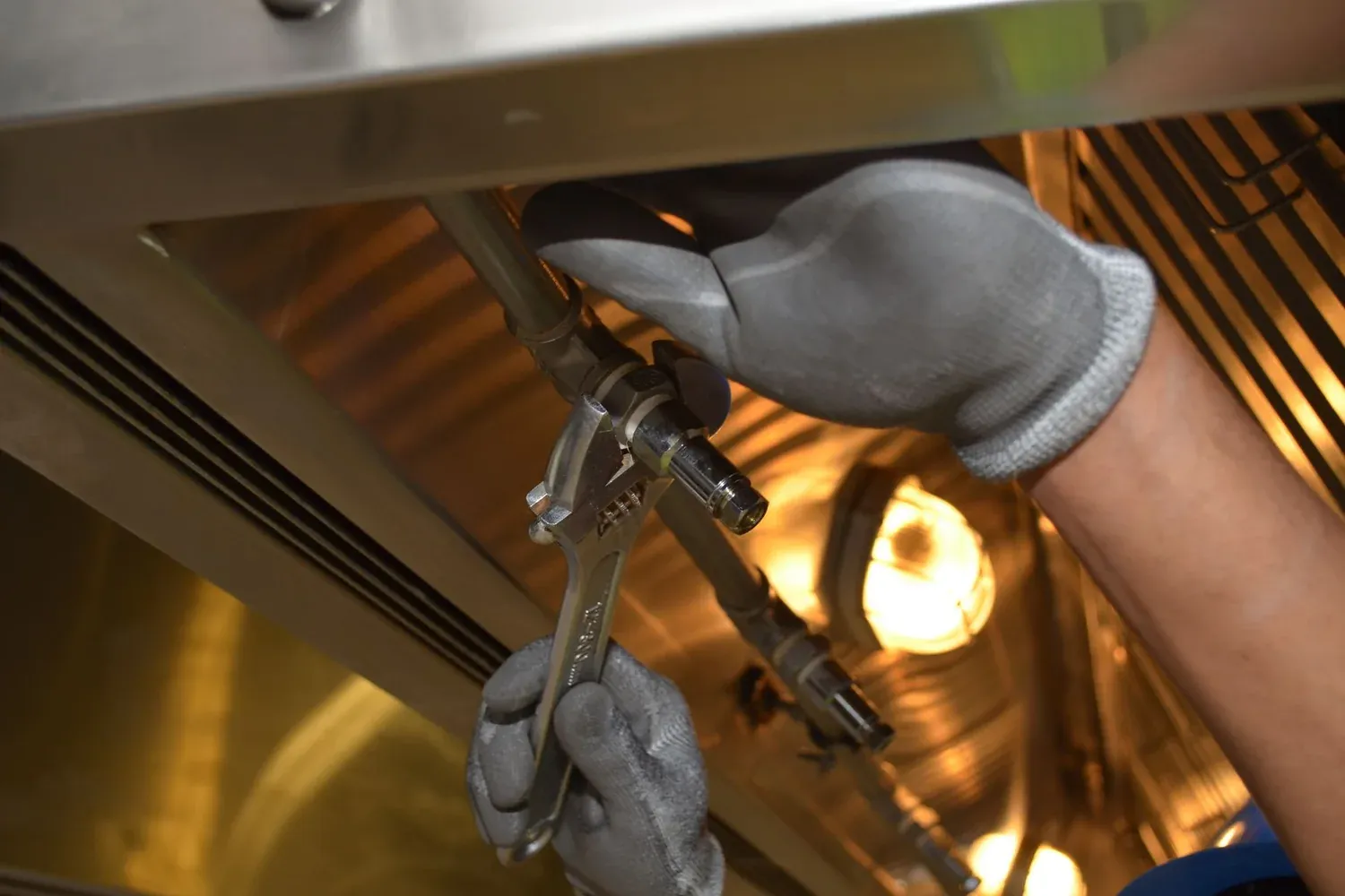 Gloved hands using a wrench to repair metal pipework